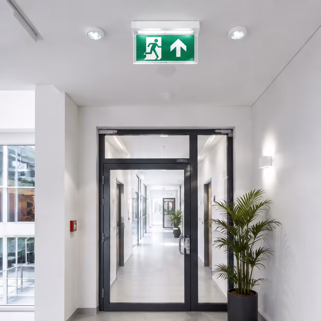 Modern corridor with an illuminated emergency exit sign showing the direction of escape.
